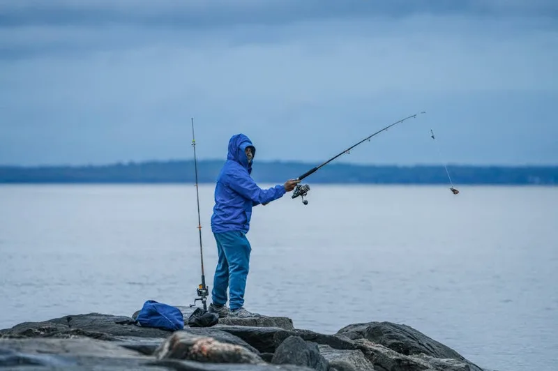 Angler casting fishing rod over calm water at sunrise