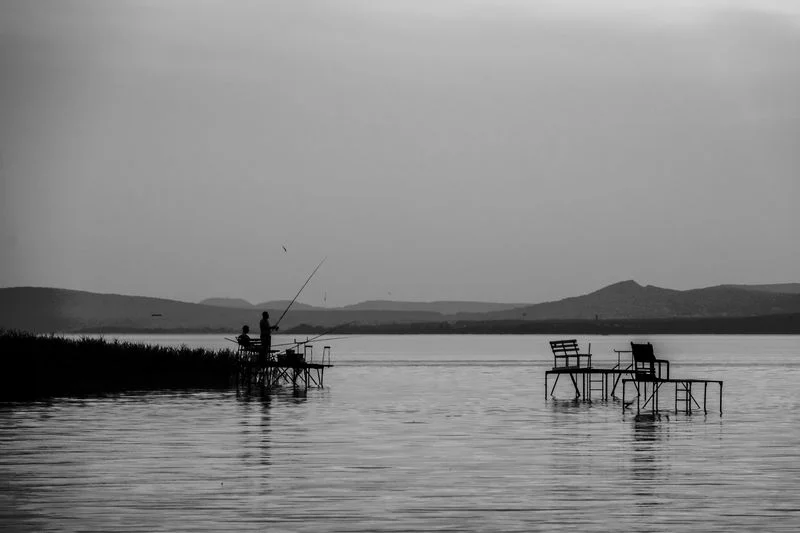 Angler casting fishing line at sunset over lake, silhouette against golden water